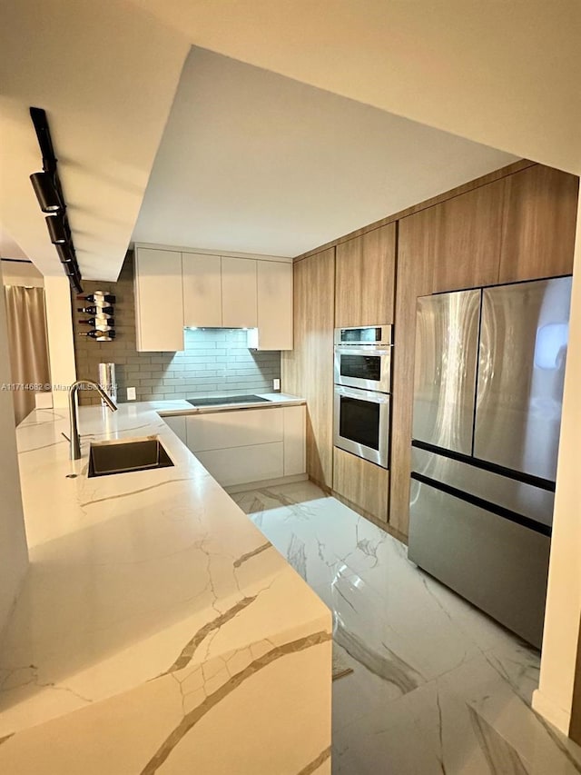 kitchen featuring light stone countertops, white cabinetry, sink, stainless steel appliances, and decorative backsplash