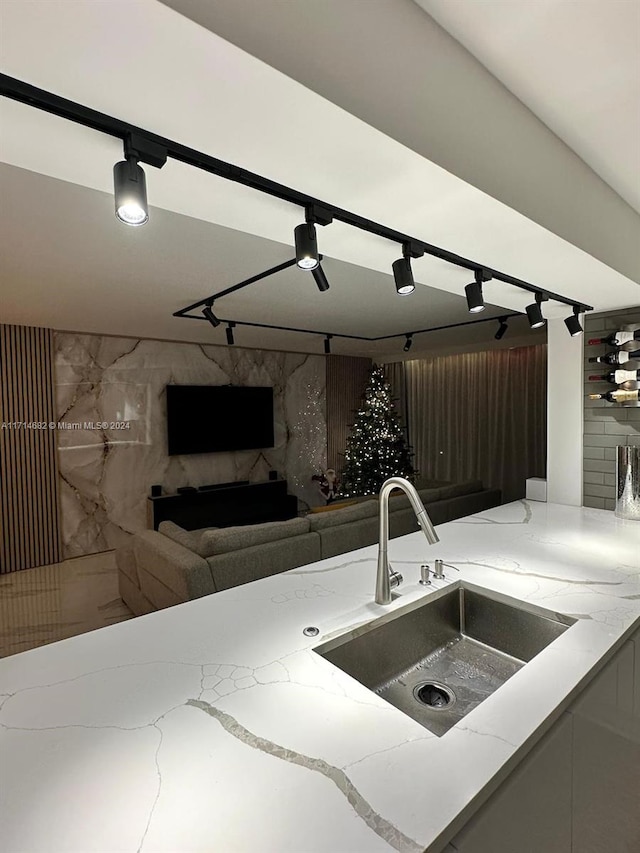 kitchen featuring track lighting, light stone counters, and sink