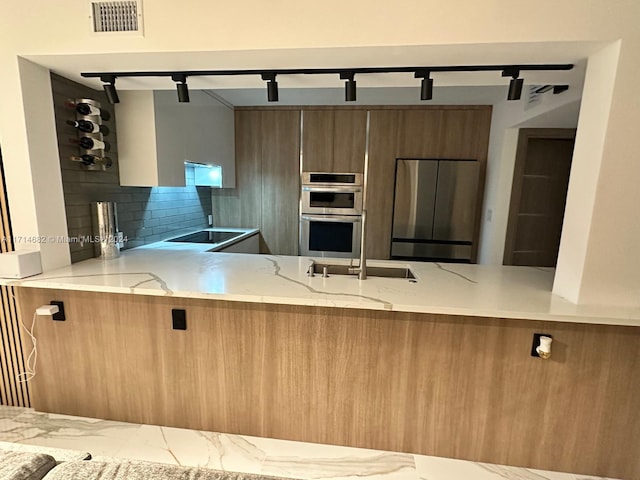 kitchen featuring sink, decorative backsplash, light stone countertops, appliances with stainless steel finishes, and kitchen peninsula