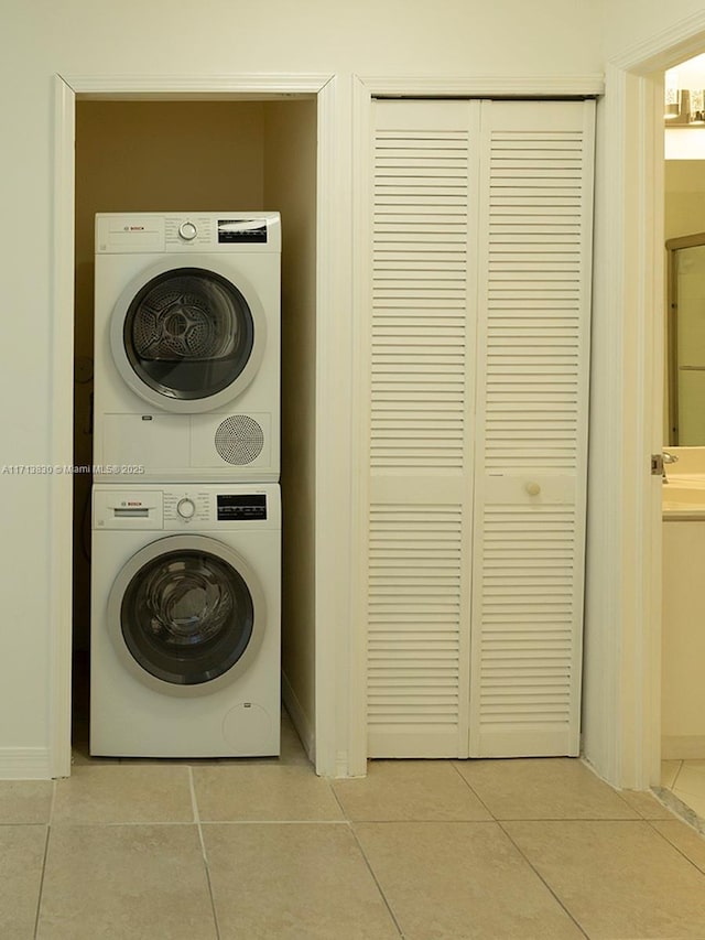 laundry room featuring stacked washing maching and dryer, sink, and light tile patterned flooring