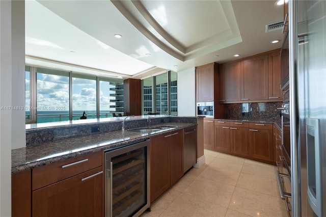 kitchen featuring a raised ceiling, wine cooler, dark stone countertops, a water view, and a sink