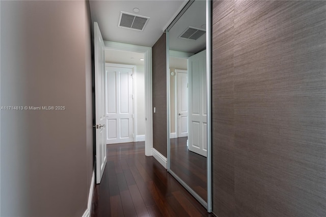 hall featuring an accent wall, visible vents, dark wood finished floors, and baseboards