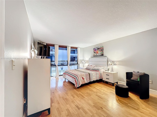 bedroom featuring hardwood / wood-style flooring, a wall of windows, a textured ceiling, and access to outside