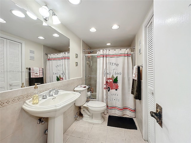 bathroom with toilet, tile patterned floors, and tile walls