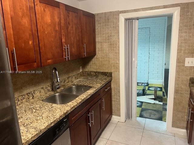 kitchen featuring sink, tile walls, light tile patterned floors, stainless steel dishwasher, and light stone countertops