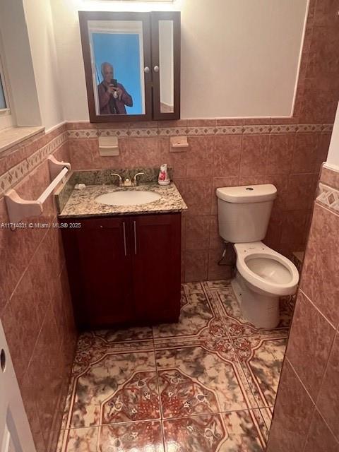 bathroom featuring tile patterned floors, toilet, vanity, and tile walls