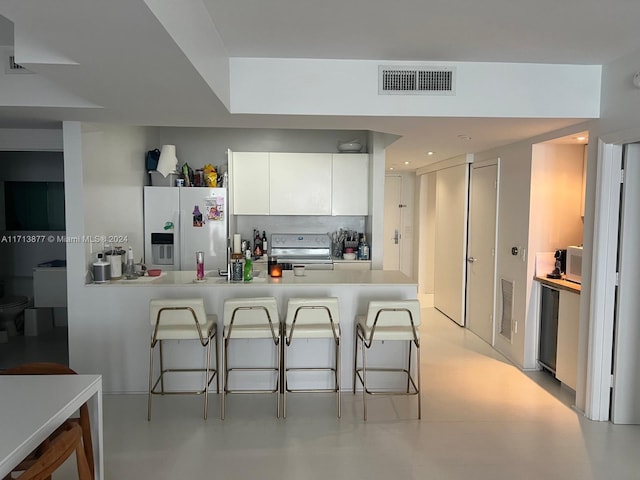 kitchen featuring kitchen peninsula, stainless steel range with electric stovetop, white cabinetry, white fridge with ice dispenser, and a breakfast bar area