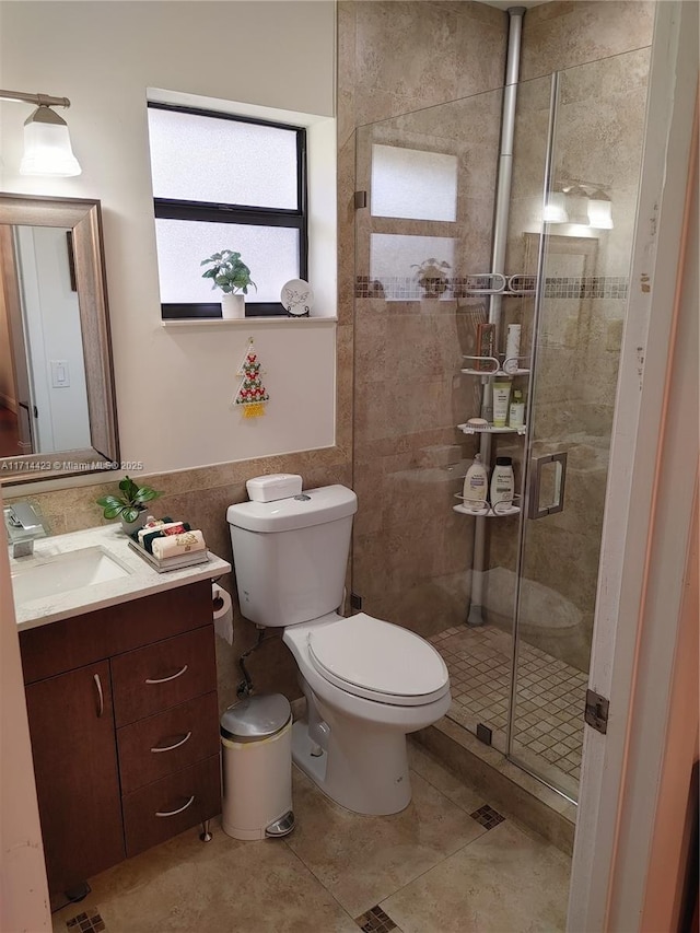 bathroom with toilet, tile walls, a shower with shower door, and vanity