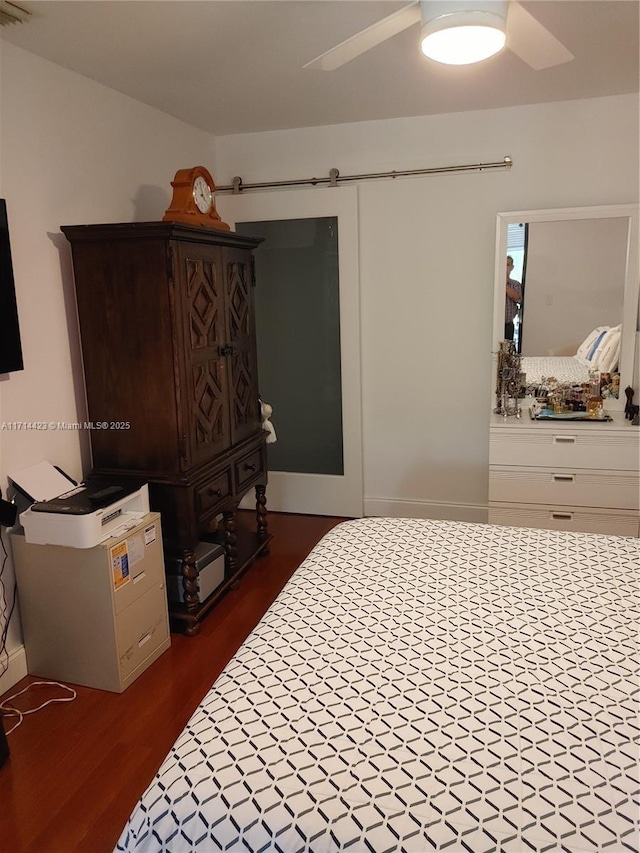 bedroom featuring dark wood-type flooring, ceiling fan, and a barn door