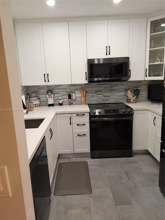 kitchen with light tile patterned floors, white cabinets, black appliances, and tasteful backsplash