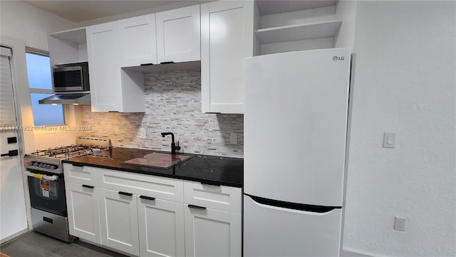 kitchen with decorative backsplash, white cabinets, ventilation hood, and appliances with stainless steel finishes