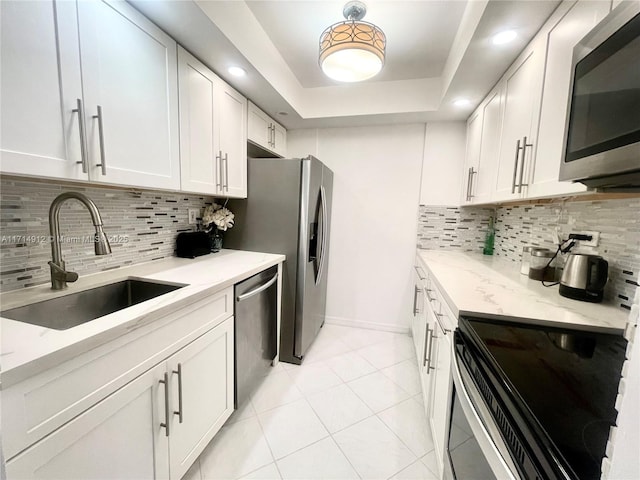 kitchen with sink, appliances with stainless steel finishes, a tray ceiling, light stone counters, and white cabinetry