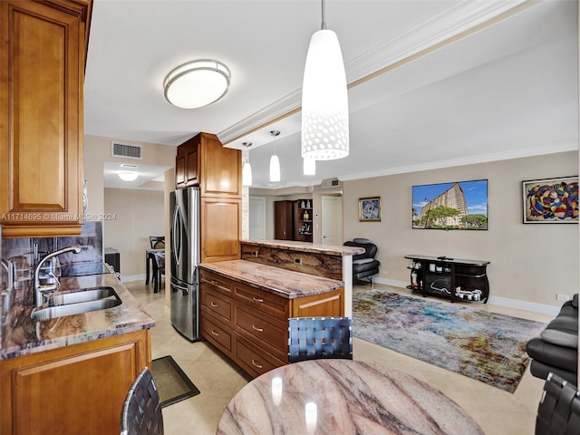 kitchen featuring stone countertops, sink, ornamental molding, decorative light fixtures, and stainless steel refrigerator