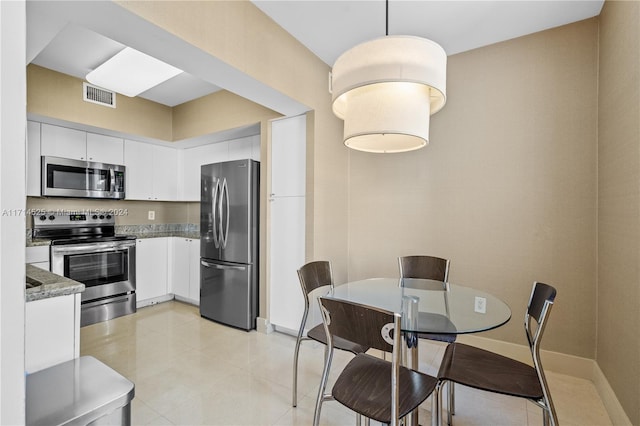 kitchen with appliances with stainless steel finishes, light stone counters, light tile patterned floors, decorative light fixtures, and white cabinets