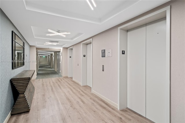 corridor featuring a tray ceiling, elevator, and light hardwood / wood-style floors