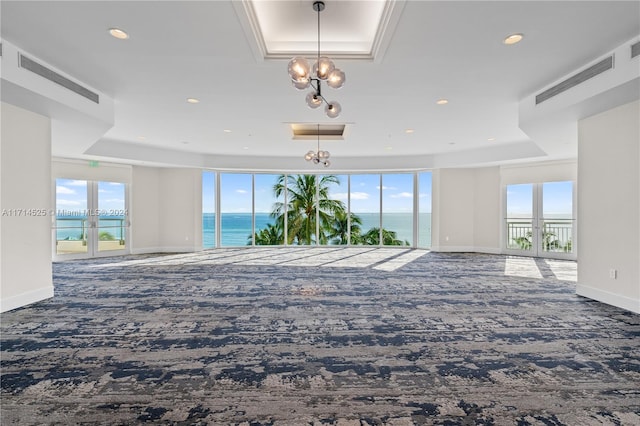 carpeted empty room with a raised ceiling, a water view, and french doors