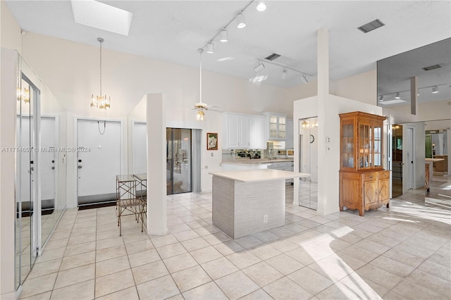 kitchen with a skylight, ceiling fan, pendant lighting, light tile patterned floors, and white cabinets