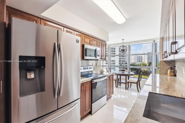 kitchen with hanging light fixtures, stainless steel appliances, light stone countertops, and tasteful backsplash