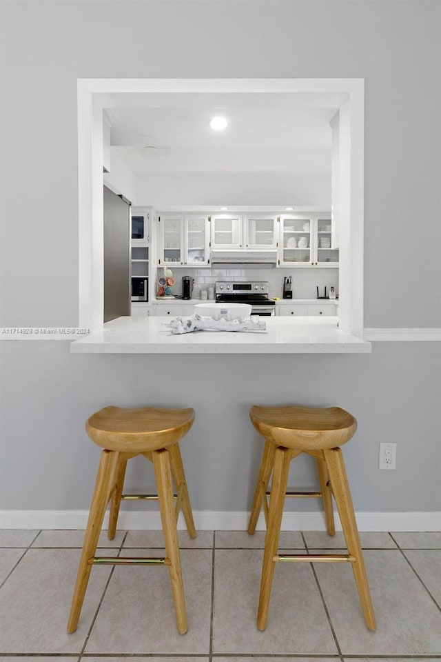 bar with white cabinets, light tile patterned floors, backsplash, and stainless steel electric range oven