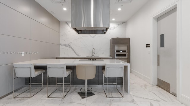 kitchen featuring sink, gray cabinetry, oven, a kitchen breakfast bar, and range hood