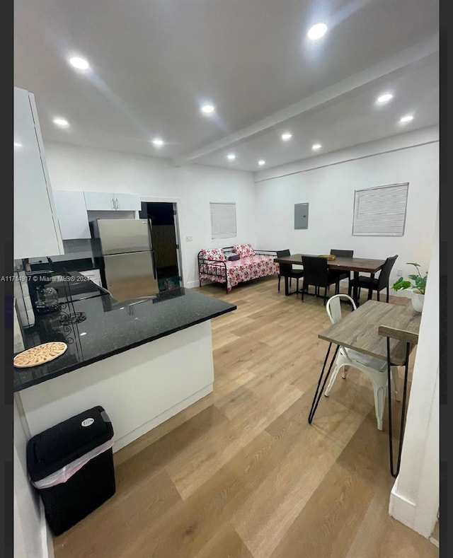 bedroom with beamed ceiling, electric panel, light hardwood / wood-style floors, and stainless steel refrigerator