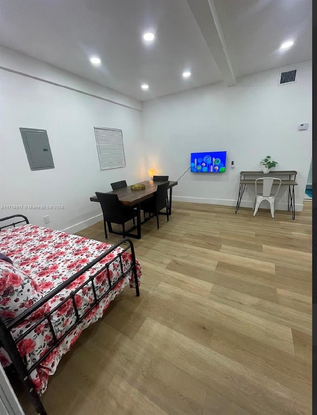 bedroom with beam ceiling, electric panel, and light hardwood / wood-style flooring