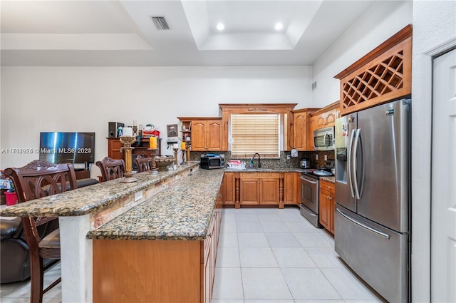 kitchen with a kitchen breakfast bar, stainless steel appliances, a tray ceiling, and sink