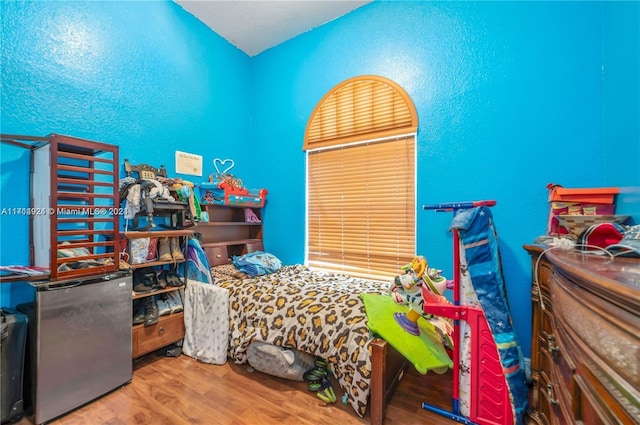 bedroom featuring hardwood / wood-style floors and refrigerator