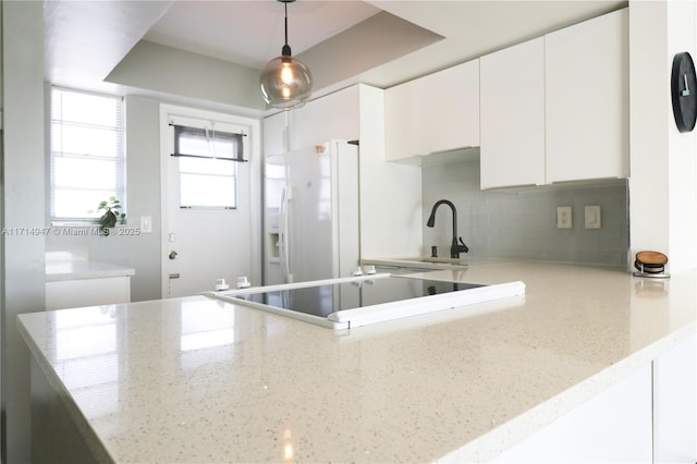 kitchen featuring kitchen peninsula, white cabinetry, white fridge with ice dispenser, and pendant lighting