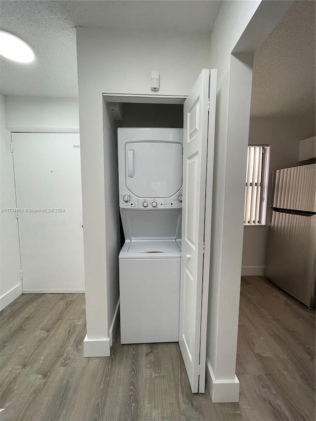 clothes washing area with a textured ceiling, hardwood / wood-style flooring, and stacked washer / drying machine