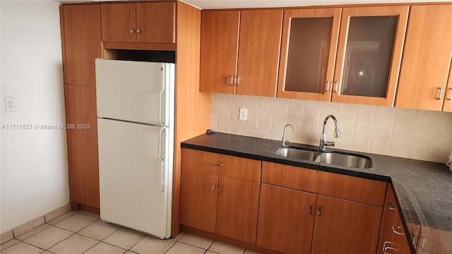 kitchen featuring sink, light tile patterned floors, dark stone countertops, backsplash, and white fridge