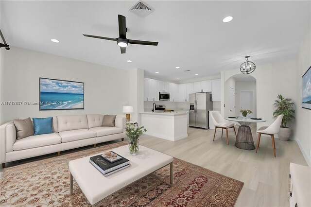 living room featuring ceiling fan with notable chandelier and light hardwood / wood-style flooring