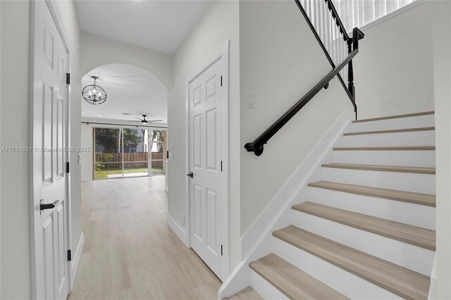 stairs featuring ceiling fan with notable chandelier and wood-type flooring