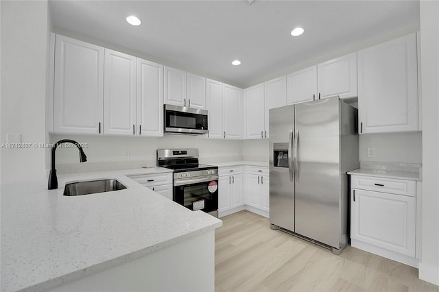 kitchen with light stone countertops, appliances with stainless steel finishes, sink, white cabinets, and light hardwood / wood-style floors