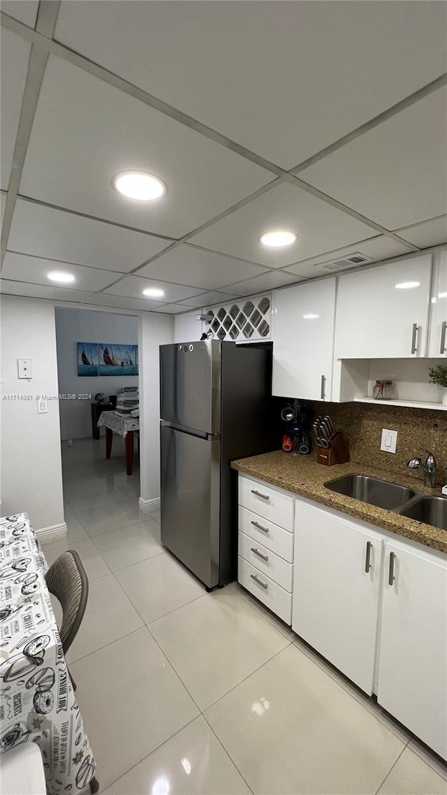 kitchen featuring dark stone counters, white cabinets, sink, light tile patterned flooring, and stainless steel refrigerator