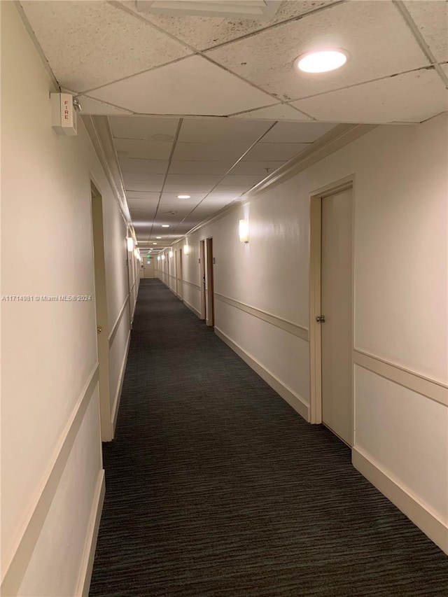 hallway with dark colored carpet and a drop ceiling