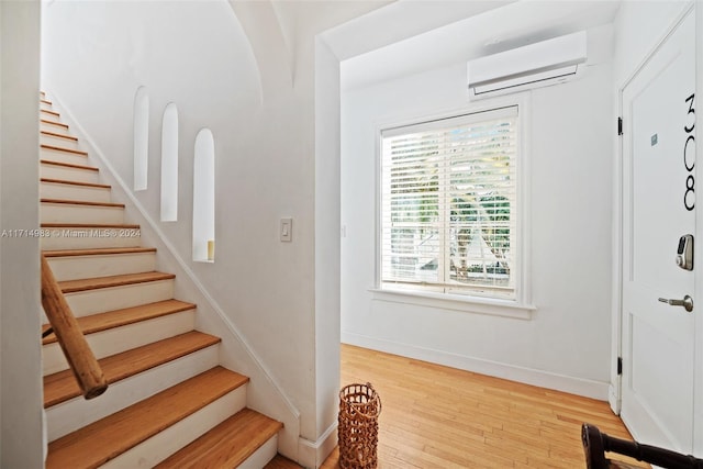 foyer entrance with a wall mounted air conditioner, light wood-type flooring, and plenty of natural light