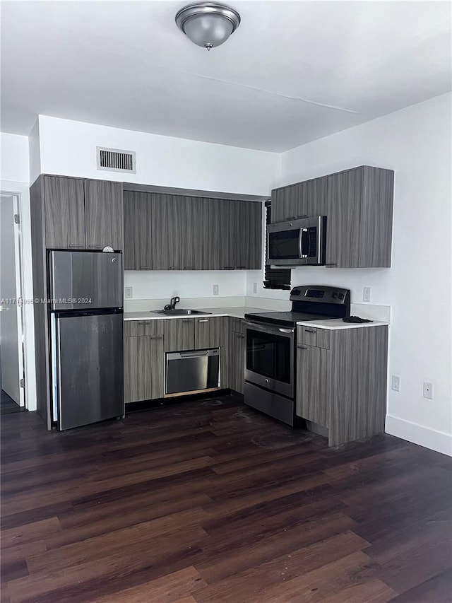 kitchen with appliances with stainless steel finishes, dark hardwood / wood-style flooring, and sink