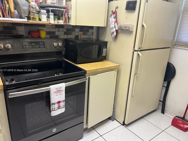 kitchen with electric range, light tile patterned flooring, freestanding refrigerator, and black microwave