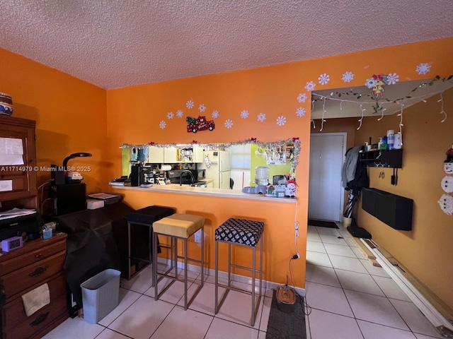 kitchen with a textured ceiling, a breakfast bar, tile patterned flooring, and freestanding refrigerator