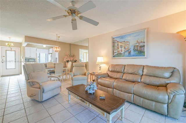 living room featuring light tile patterned floors, ceiling fan with notable chandelier, and a textured ceiling