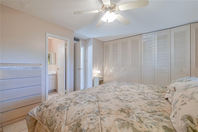 tiled bedroom with connected bathroom, ceiling fan, a closet, and a textured ceiling