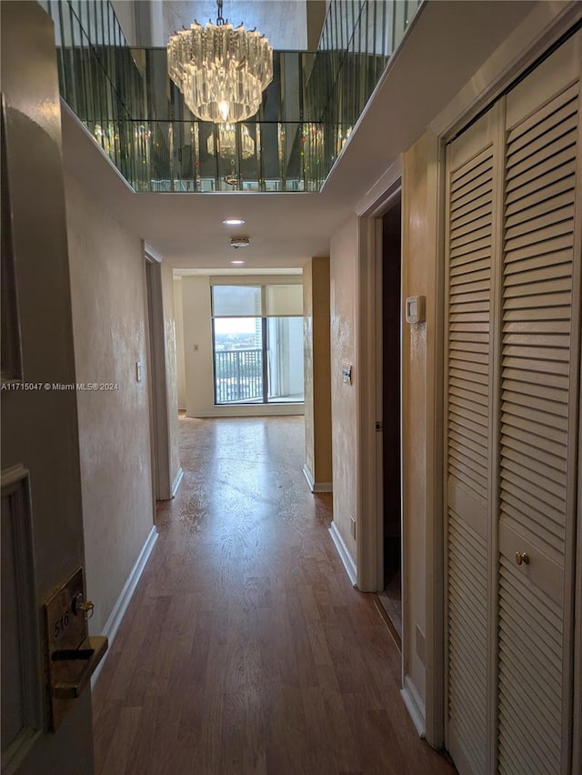 corridor featuring hardwood / wood-style floors, a towering ceiling, and an inviting chandelier