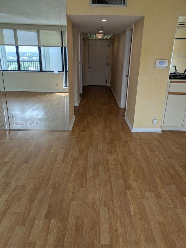 hallway with light wood-type flooring and a textured ceiling