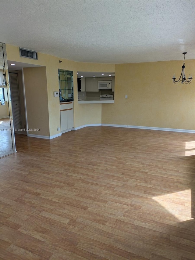 unfurnished living room with light wood-type flooring, a textured ceiling, and a notable chandelier