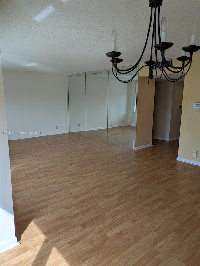 unfurnished room with light hardwood / wood-style floors, a textured ceiling, and an inviting chandelier