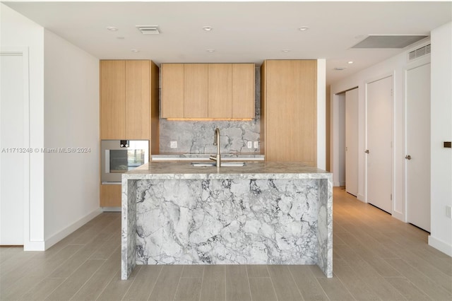 kitchen featuring backsplash, stainless steel oven, sink, and light brown cabinetry