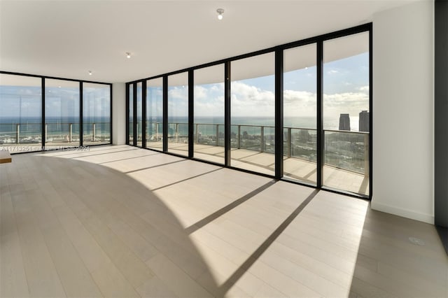 empty room with hardwood / wood-style flooring, a water view, and a wall of windows