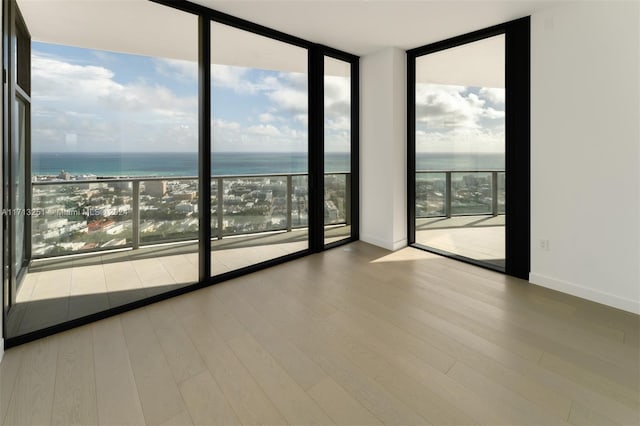 empty room with a water view, light hardwood / wood-style floors, a view of the beach, and a wall of windows