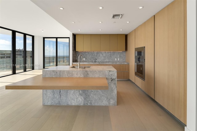 kitchen featuring light brown cabinets, sink, decorative backsplash, a large island, and a wall of windows